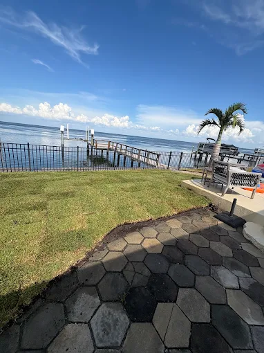 Waterfront lawn with fresh sod beside a paver patio and dock